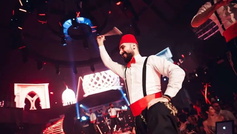 Dabke dancer in a red fez waving a handkerchief on stage at a Dubai venue
