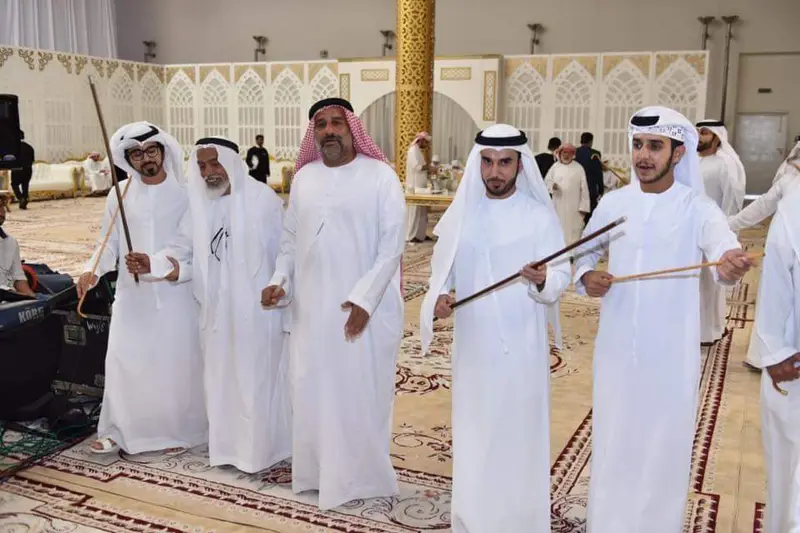 Men in white kandura dancing the ayala with thin canes in a wedding hall in the UAE