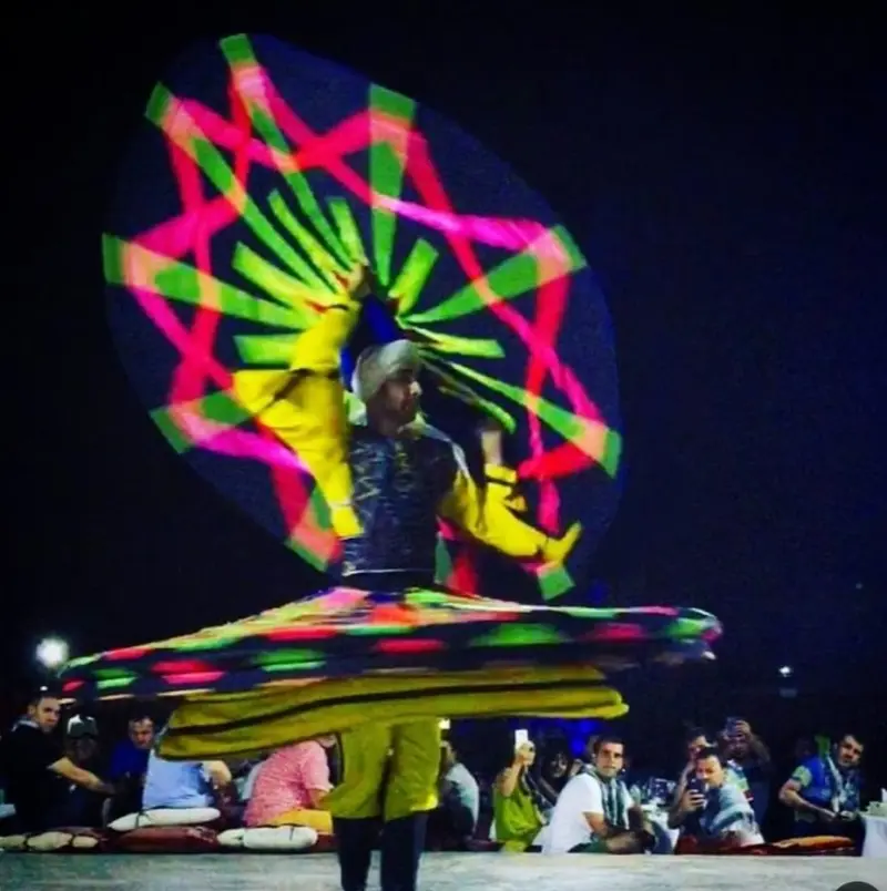 Tanoura dancer spinning a bright multicoloured skirt in front of seated guests at an evening show